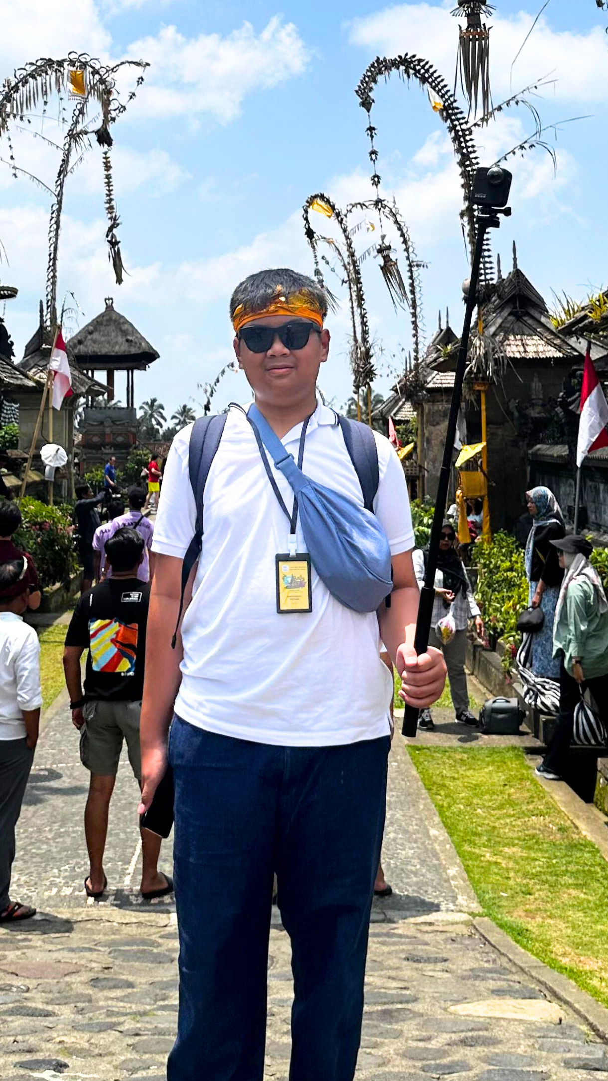 Foto saya di Desa Penglipuran, tersenyum, membawa kamera stick 360º, sambil memakai aksesoris Bali dan kacamata hitam.
