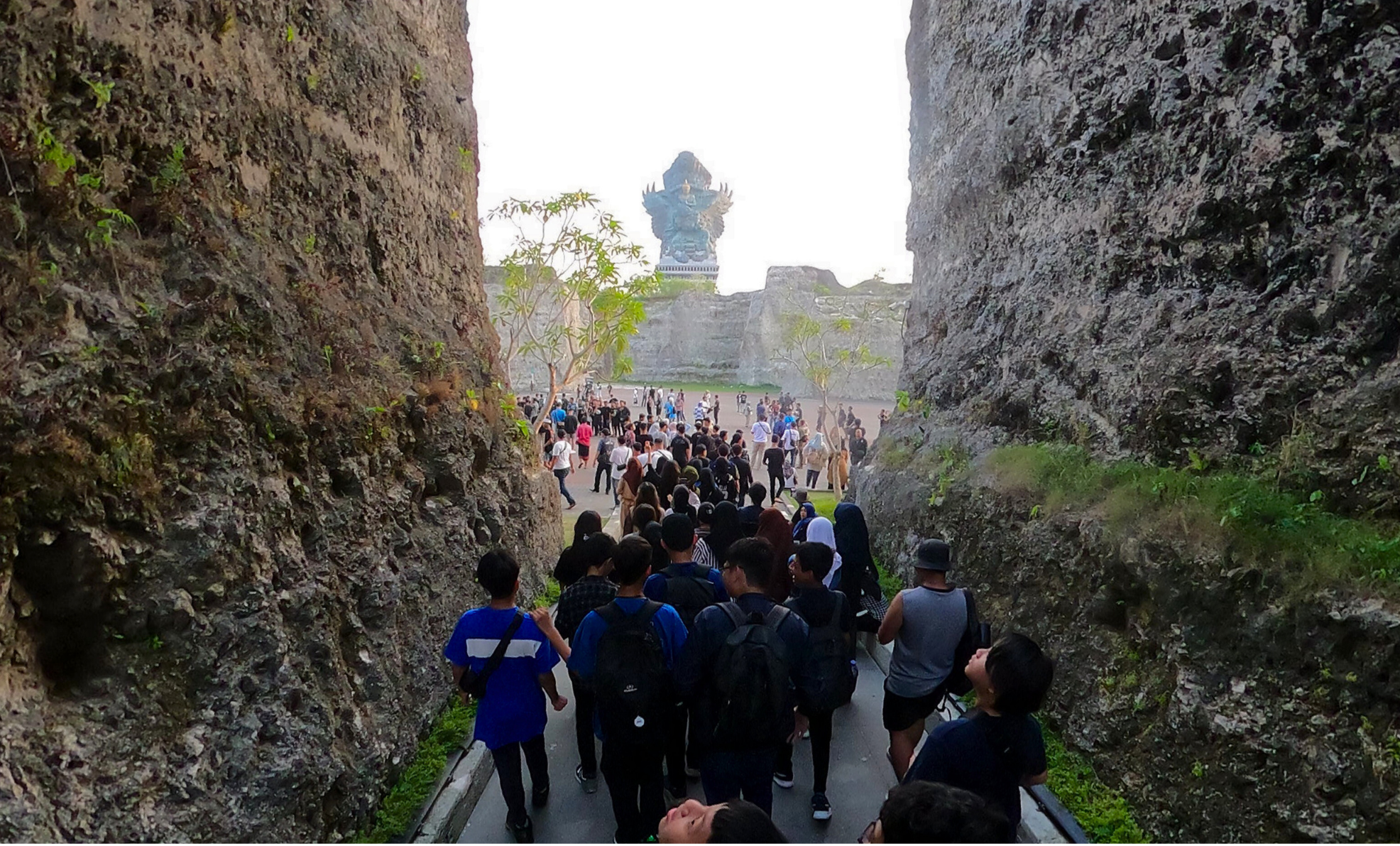 Foto di Patung Garuda Wisnu Kencana dari jarak jauh di sela-sela bebatuan raksasa.